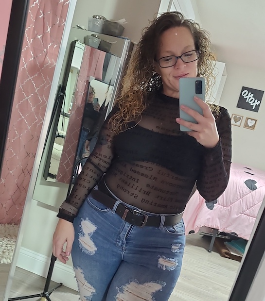 Selfie photo of Rayna wearing a black sheer top and ripped jeans